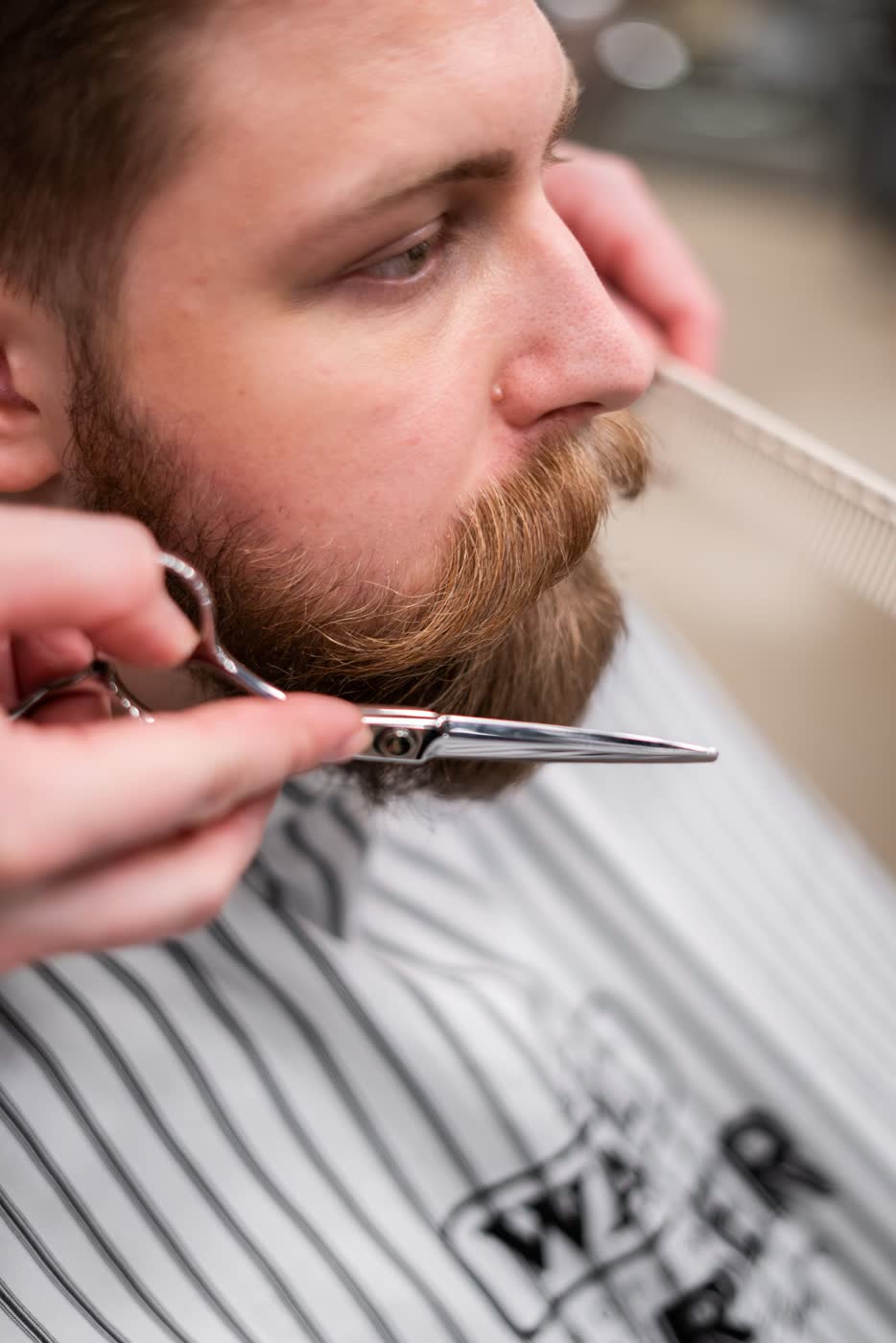 Barber trimming a beard with scissors and comb